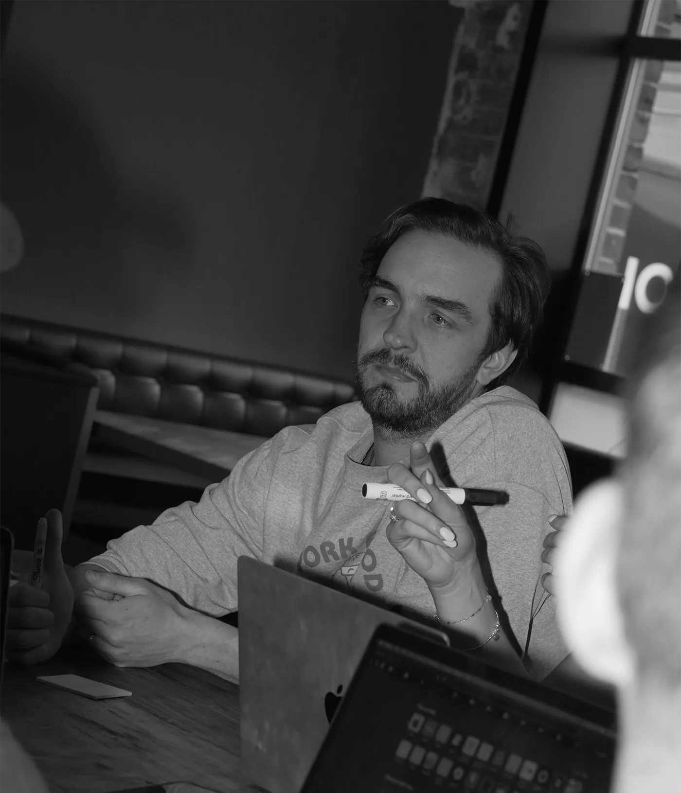 Black-and-white photo of Kieran Link in a workshop, sitting at a table with laptops.